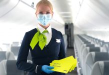 Бортпроводник airBaltic с защитным набором для пассажиров, который включает маску и дезинфицирующую салфетку