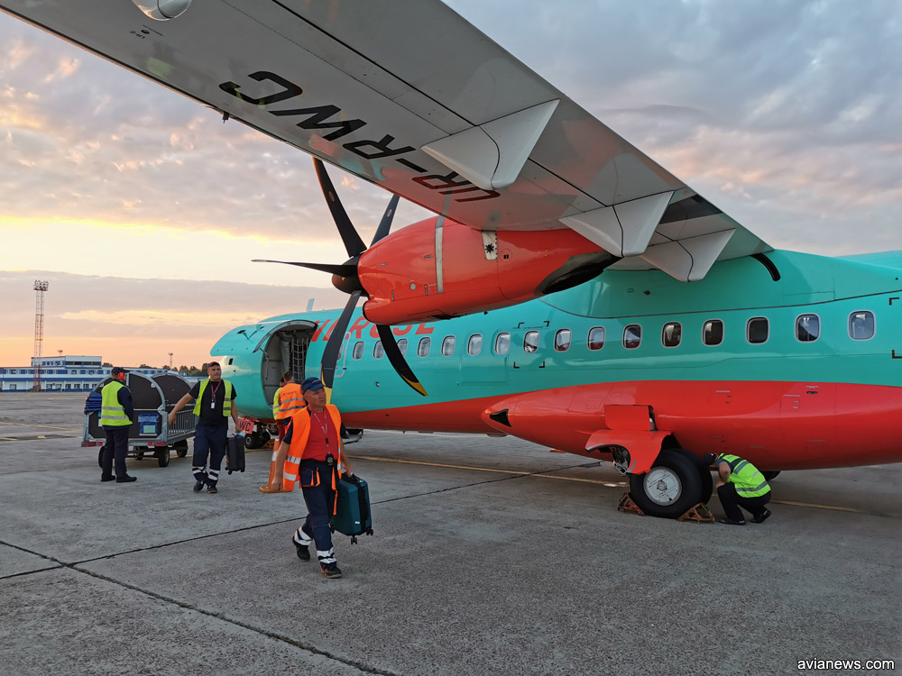 Выгрузка большой ручной клади из ATR 72-600 в аэропорту. Передается пассажирам у трапа самолета по прилету