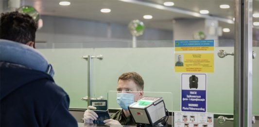 Пограничник в маске проверяет паспорт пассажира