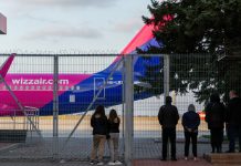 Люди наблюдают за самолетом Wizz Air через забор